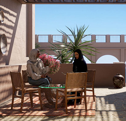 Two women seated at an outdoor table in a shaded Middle Eastern courtyard with tropical plants