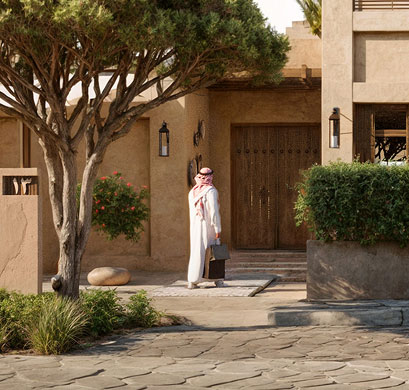 Man in a thobe walking to the wooden entrance of a Khaleeji-style home