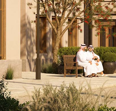 Two men in thobes talking on a bench in a shaded residential courtyard